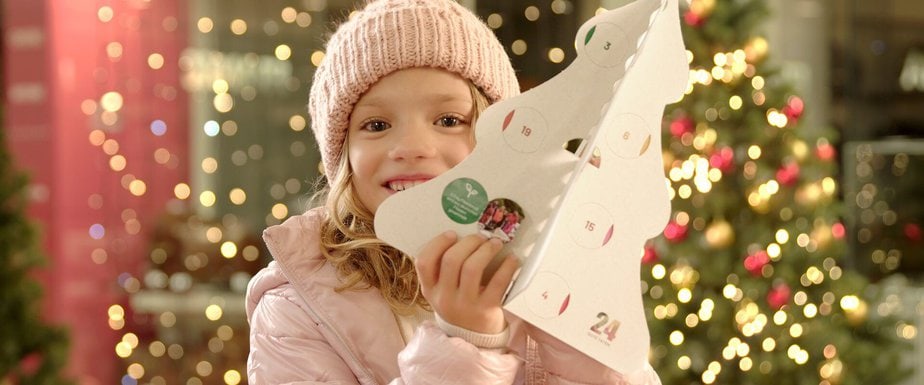 little girl in winter hat and coat holds advent calendar in the shape of a christmas tree