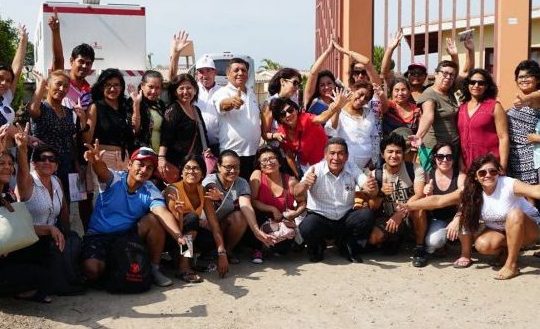 A group of Peruvians wave and smile outside a school.