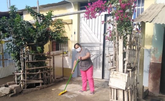 Woman in mask sweeping entrance to her home.