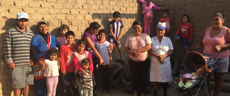 Mothers and children stand in front of an adobe wall