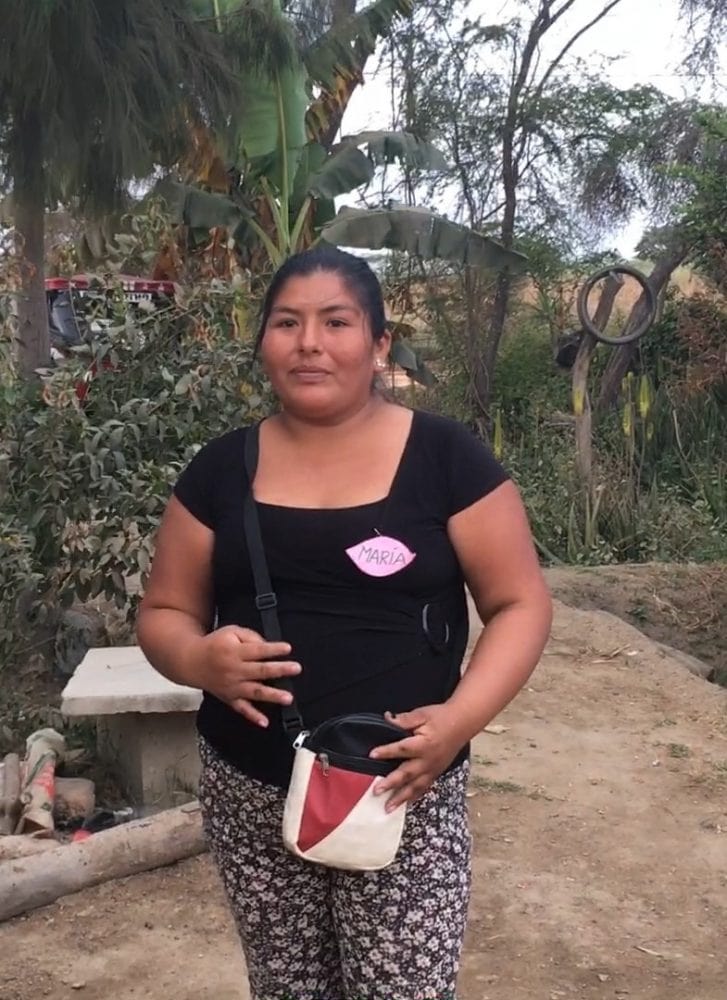Woman with black T and small purse over her shoulder stands in Peruvian farmyard