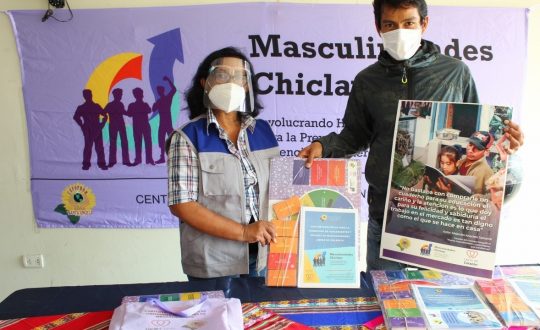 A man and a woman in masks display a poster and educational materials for teaching new masculinities