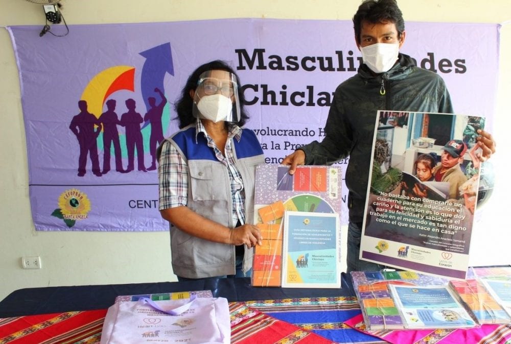 A man and a woman in masks display a poster and educational materials for teaching new masculinities