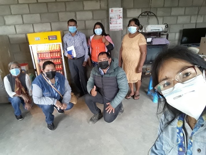 woman takes selfie with six other people in the background kneeling or standing in front of an upright chicken incubator