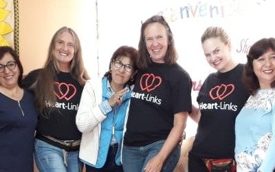 eight people, three wearing Heart-Links T-shirst, , stand arm in arm kicking out their right or left foot