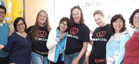 eight people, three wearing Heart-Links T-shirst, , stand arm in arm kicking out their right or left foot