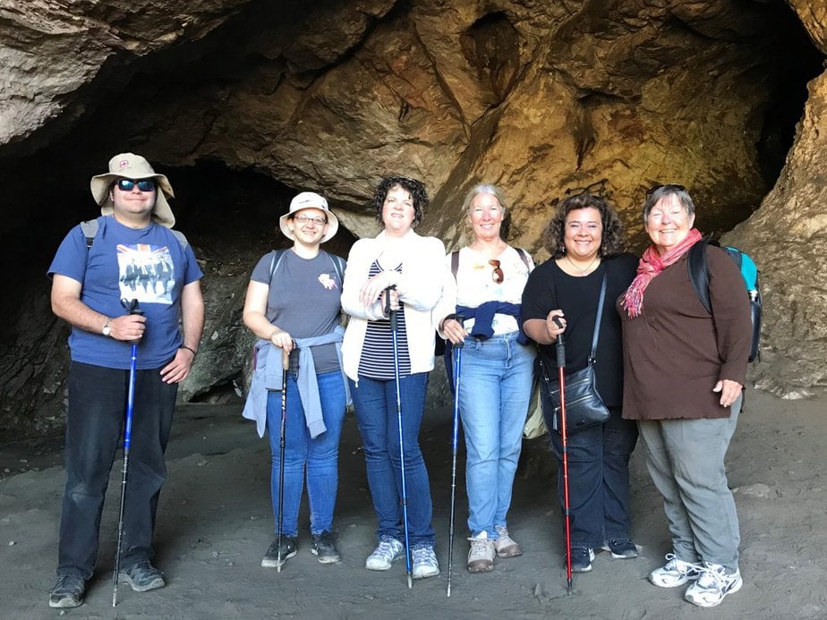 6 hikers stand with hiking poles in from of a cave