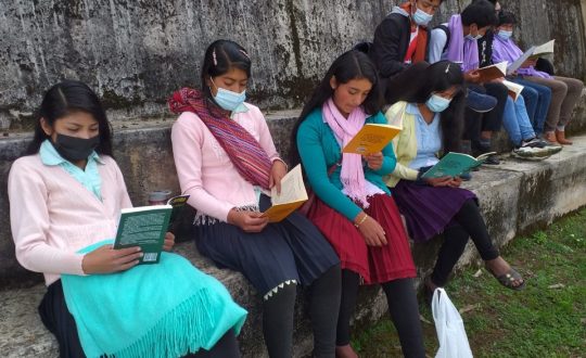 four indigenous girls sit along wall reading