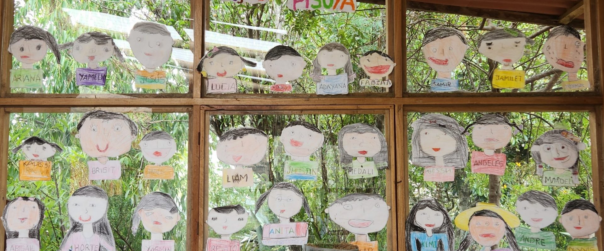 A window with wooden frame covered with cut-outs of children's self-portraits on paper.