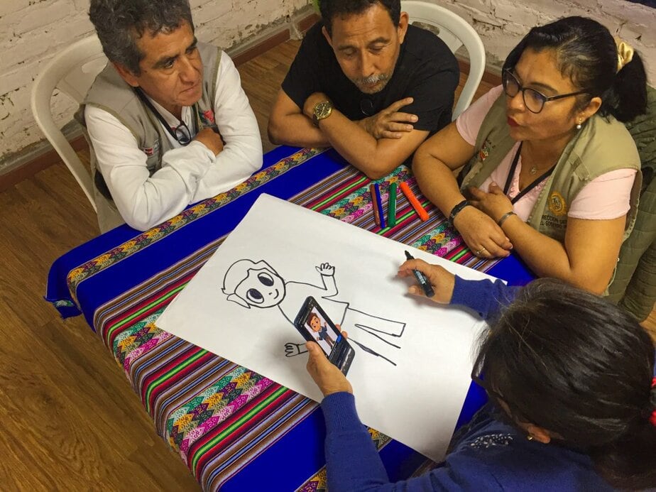 two men and two women sit at a table looking a a drawing of a man