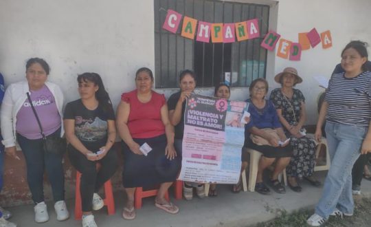 women sit and stand against a wall holding a sign calling for the end of violence against women